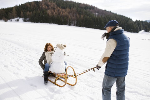 Älteres Paar mit Schneemann auf Schlitten in Winterlandschaft, lizenzfreies Stockfoto