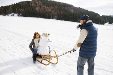 Senior couple with snowman on sledge in winter landscape - HAPF02273