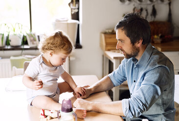 Father playing with little boy sitting on kitchen table - HAPF02283