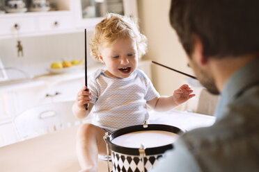 Vater mit fröhlichem kleinen Jungen, der auf dem Küchentisch sitzt und Trommel spielt - HAPF02285