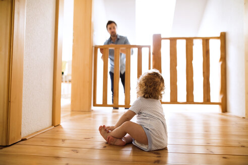 Ein kleiner Junge sitzt auf dem Holzboden und sieht seinen Vater hinter der Absperrung an der Treppe an - HAPF02290