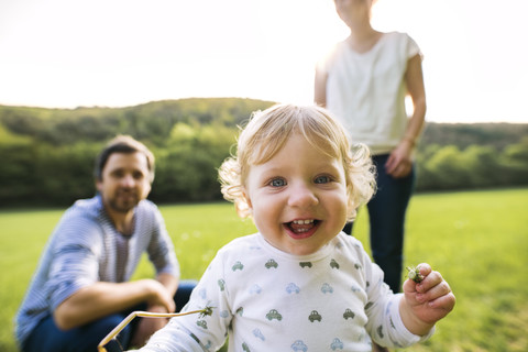 Niedlicher kleiner Junge auf Wiese mit Eltern im Hintergrund, lizenzfreies Stockfoto