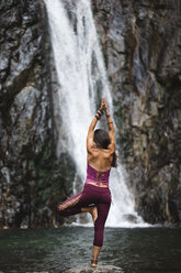 Italy, Lecco, woman doing Tree Yoga Pose on a rock near a waterfall - MRAF00251