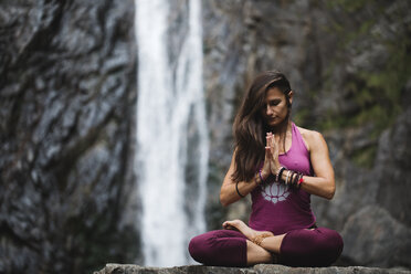 Italien, Lecco, Frau beim Meditieren an einem Wasserfall - MRAF00255