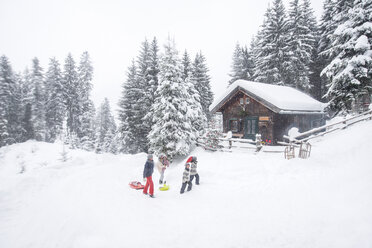 Österreich, Altenmarkt-Zauchensee, Familie mit Schlitten am Holzhaus zur Weihnachtszeit - HHF05488