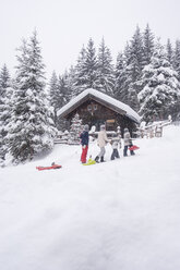 Österreich, Altenmarkt-Zauchensee, Familie mit Schlitten am Holzhaus zur Weihnachtszeit - HHF05489