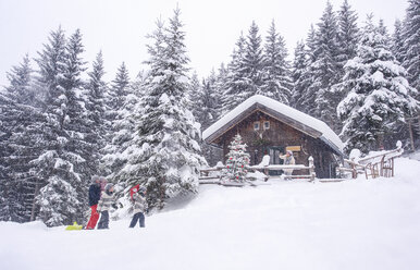 Österreich, Altenmarkt-Zauchensee, Familie mit Schlitten am Holzhaus zur Weihnachtszeit - HHF05490