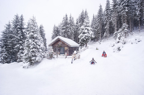 Österreich, Altenmarkt-Zauchensee, Familienrodeln am Holzhaus zur Weihnachtszeit, lizenzfreies Stockfoto