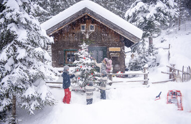 Österreich, Altenmarkt-Zauchensee, Familie schmückt Weihnachtsbaum in Holzhaus - HHF05494