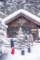 Austria, Altenmarkt-Zauchensee, family decorating Christmas tree at wooden house - HHF05495