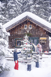 Österreich, Altenmarkt-Zauchensee, Familie schmückt Weihnachtsbaum in Holzhaus - HHF05495