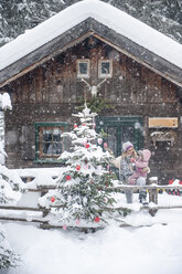 Österreich, Altenmarkt-Zauchensee, Mutter mit kleinem Sohn beim Schmücken des Weihnachtsbaums am Holzhaus - HHF05497