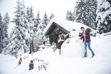 Austria, Altenmarkt-Zauchensee, friends building up big snowman at wooden house - HHF05499