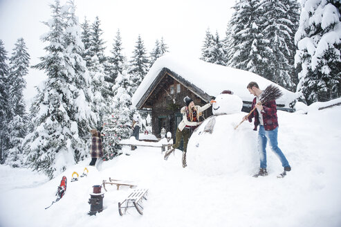 Österreich, Altenmarkt-Zauchensee, Freunde bauen einen großen Schneemann am Holzhaus - HHF05499