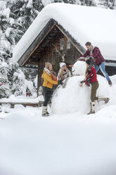 Österreich, Altenmarkt-Zauchensee, Freunde bauen einen großen Schneemann am Holzhaus - HHF05502