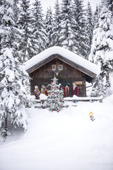 Austria, Altenmarkt-Zauchensee, friends decorating Christmas tree at wooden house - HHF05505