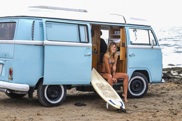 Porträt einer glücklichen jungen Frau mit Surfbrett im Van am Strand - SIPF01799