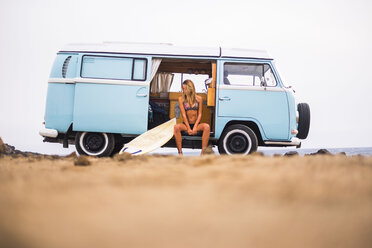 Young woman with surfboard sitting in van on the beach - SIPF01803