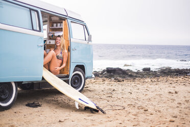 Laughing young woman with surfboard in van on the beach - SIPF01805