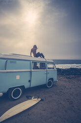 Young woman sitting on roof of a van on the beach - SIPF01809