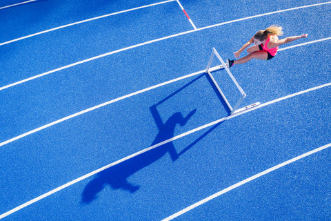 Top view of female runner crossing hurdle on tartan track stock photo