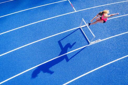 Top view of female runner crossing hurdle on tartan track - STSF01331