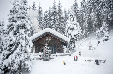 Österreich, Altenmarkt-Zauchensee, Schneemann, Schlitten und Weihnachtsbaum am Holzhaus im Schnee - HHF05510