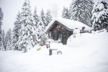 Austria, Altenmarkt-Zauchensee, snowman, sledges and Christmas tree at wooden house in snow - HHF05512