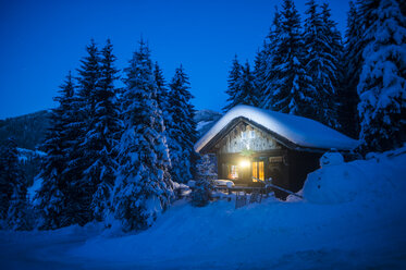 Austria, Altenmarkt-Zauchensee, sledges, snowman and Christmas tree at illuminated wooden house in snow at night - HHF05514