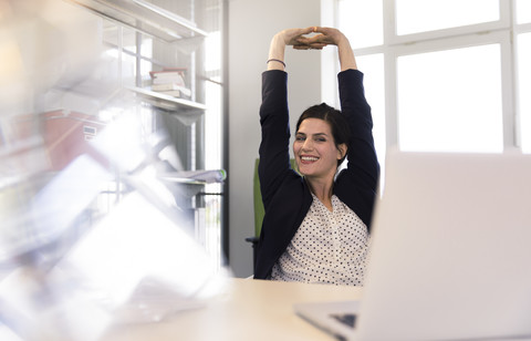 Glückliche Geschäftsfrau sitzt im Büro, schaut auf den Laptop, streckt sich, lizenzfreies Stockfoto