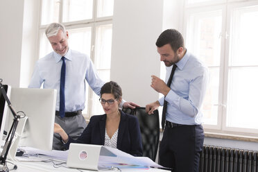 Colleagues standing in office, discussing blueprints - FKF02629