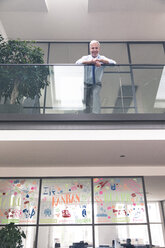 Successful businessman standing at railing in his office - FKF02655