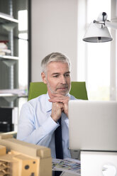 Businessman working in office, using laptop - FKF02664