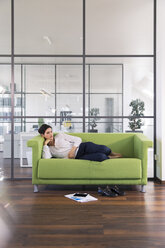 Geschäftsfrau macht ein Nickerchen auf einer Couch im Büro liegend - FKF02709