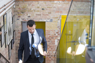 Young businessman in a suit carrying longboard, climbing stairs - FKF02726