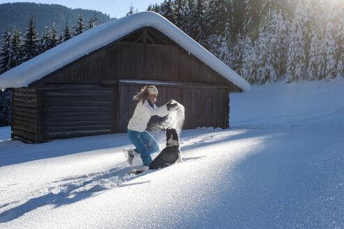 Österreich, Altenmarkt-Zauchensee, glückliche junge Frau spielt mit Hund im Schnee - HHF05517