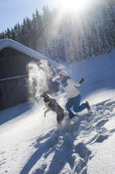 Österreich, Altenmarkt-Zauchensee, glückliche junge Frau spielt mit Hund im Schnee - HHF05518