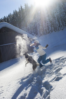 Austria, Altenmarkt-Zauchensee, happy young woman playing with dog in snow - HHF05518
