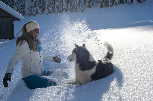 Österreich, Altenmarkt-Zauchensee, glückliche junge Frau spielt mit Hund im Schnee - HHF05519