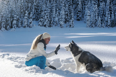 Austria, Altenmarkt-Zauchensee, young woman sitting with dog in snow - HHF05520