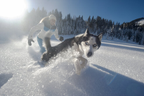 Österreich, Altenmarkt-Zauchensee, glückliche junge Frau läuft mit Hund im Schnee - HHF05522