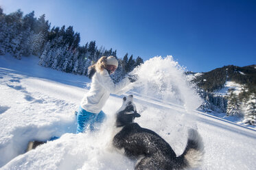 Österreich, Altenmarkt-Zauchensee, glückliche junge Frau spielt mit Hund im Schnee - HHF05523