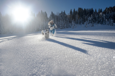 Austria, Altenmarkt-Zauchensee, happy young woman running with dog in snow stock photo