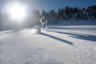 Österreich, Altenmarkt-Zauchensee, glückliche junge Frau läuft mit Hund im Schnee - HHF05524