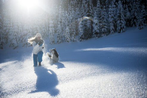 Österreich, Altenmarkt-Zauchensee, glückliche junge Frau läuft mit Hund im Schnee - HHF05525