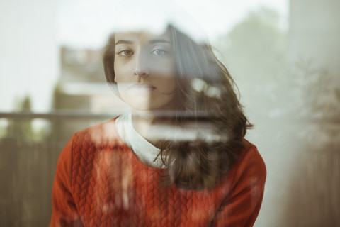 Porträt einer ernsten jungen Frau hinter einer Glasscheibe, lizenzfreies Stockfoto