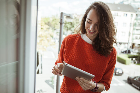 Smiling young woman holding tablet on balcony - FEXF00292