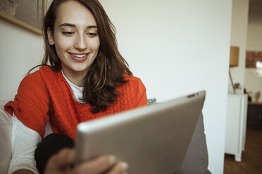 Smiling young woman holding tablet on couch - FEXF00293