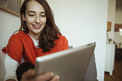 Smiling young woman holding tablet on couch - FEXF00293