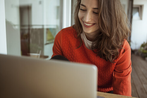 Lächelnde junge Frau mit Laptop auf dem Balkon - FEXF00296